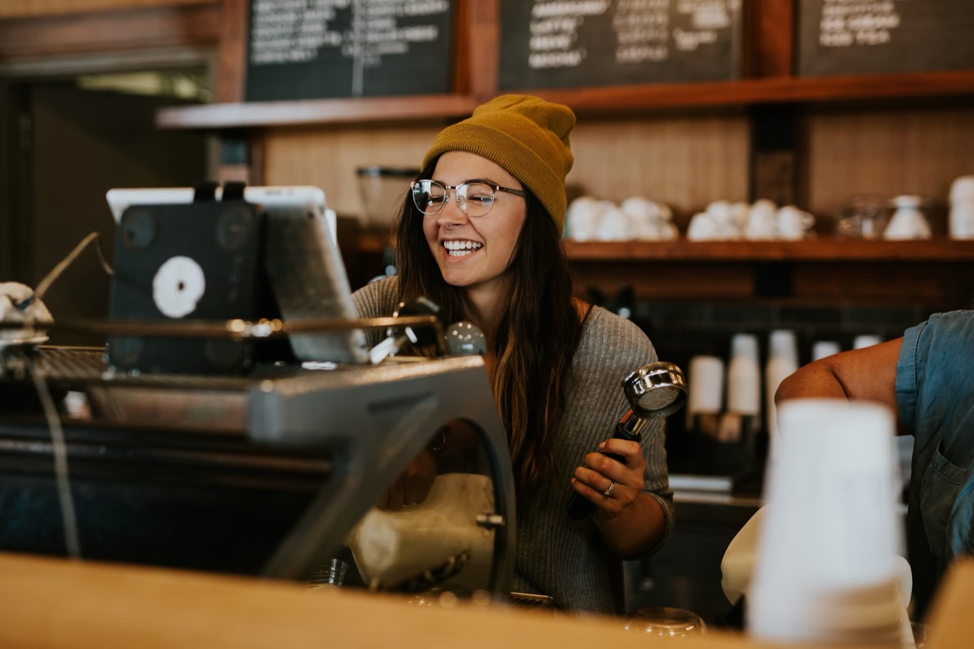 A local coffee shop owner smiling behind her espresso machine
